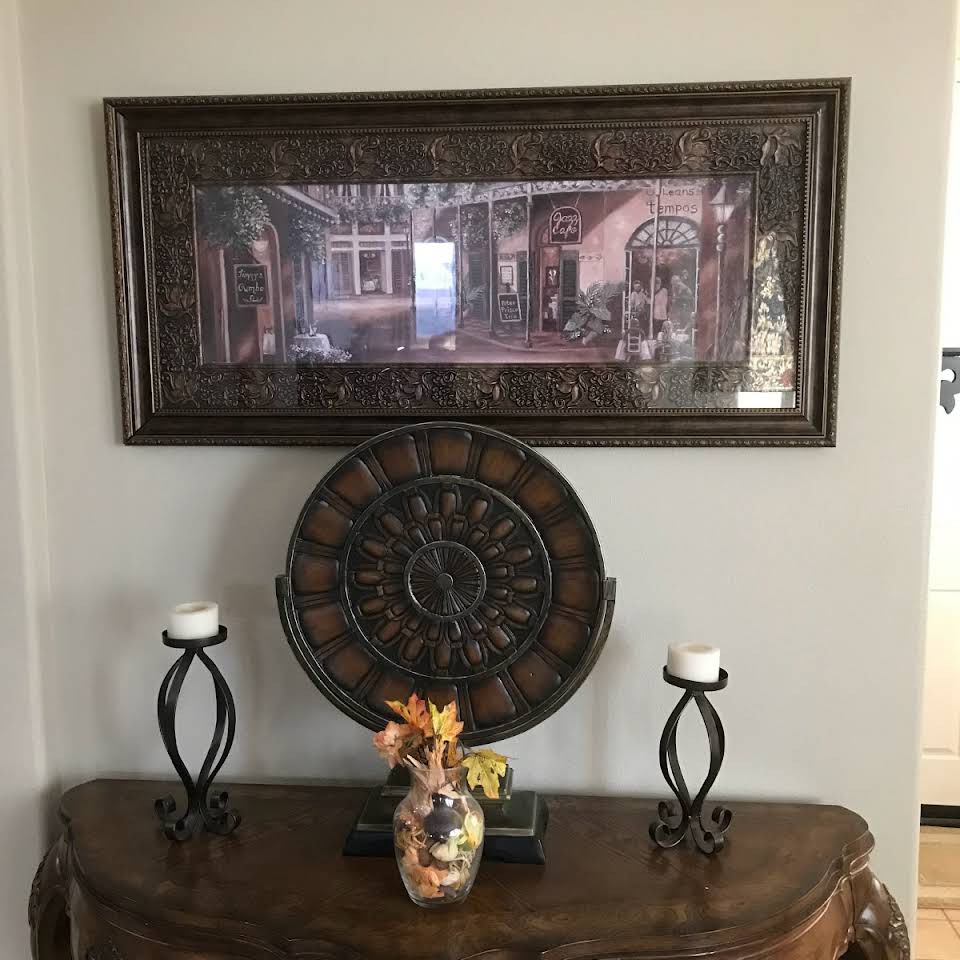 A tastefully decorated console table featuring a framed artwork, flanked by two candles and a vase with flowers.