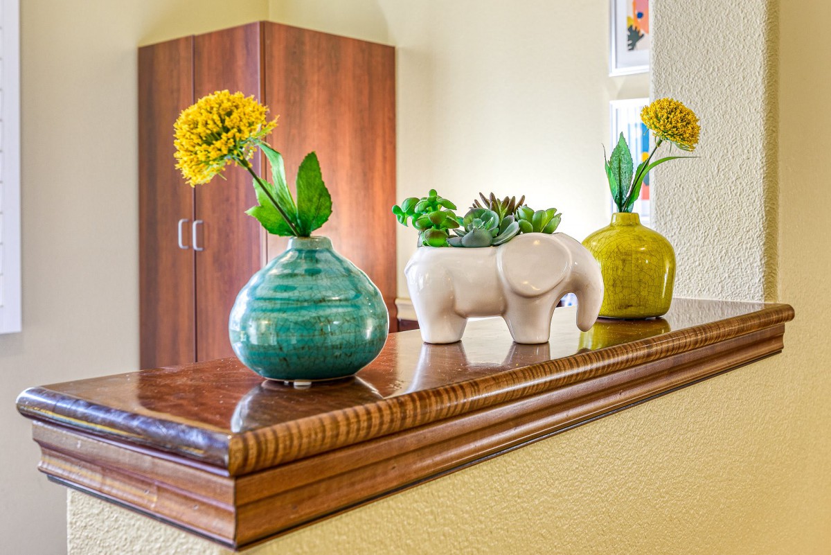 A decorative setup featuring colorful vases with flowers and a white elephant planter with succulents, arranged on a polished wooden surface.