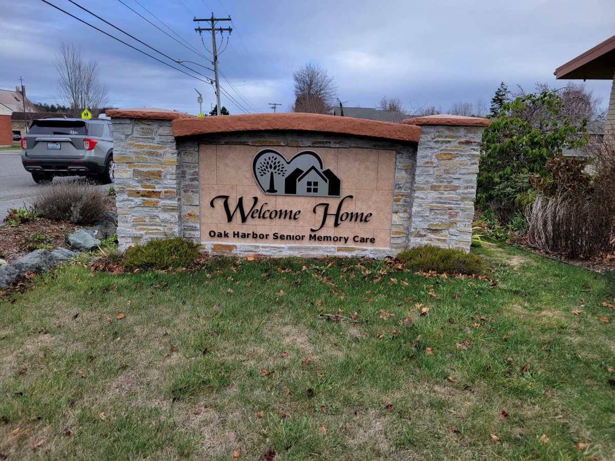 A stone sign for a building with the name 'Welcome Home' surrounded by grass and trees.