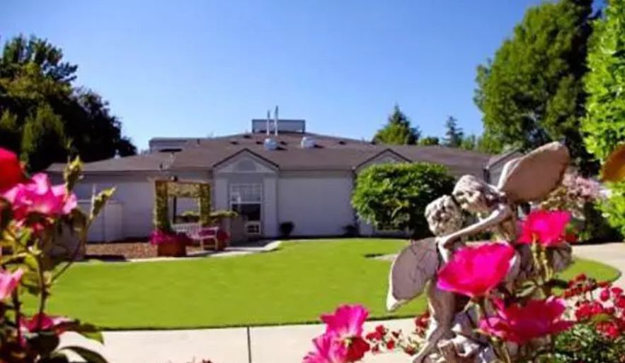 A well-maintained garden with a sculpture and vibrant flowers in front of a house.