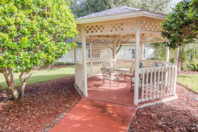 A charming garden gazebo with patio furniture, surrounded by lush greenery on a sunny day.