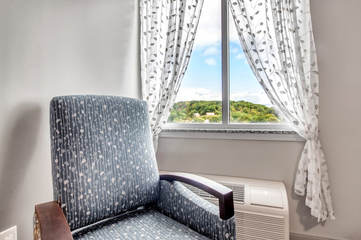 A cozy chair by the window with patterned curtains, offering a scenic view outside.