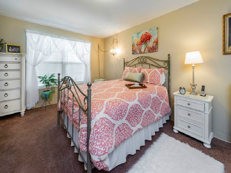 A cozy bedroom with a stylish bed adorned with pink bedding, a bedside lamp on a white nightstand, and artwork on the wall.