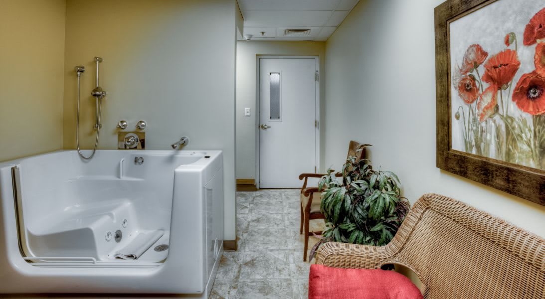 A hallway with seating, plants, a bathtub, and a door at the end.