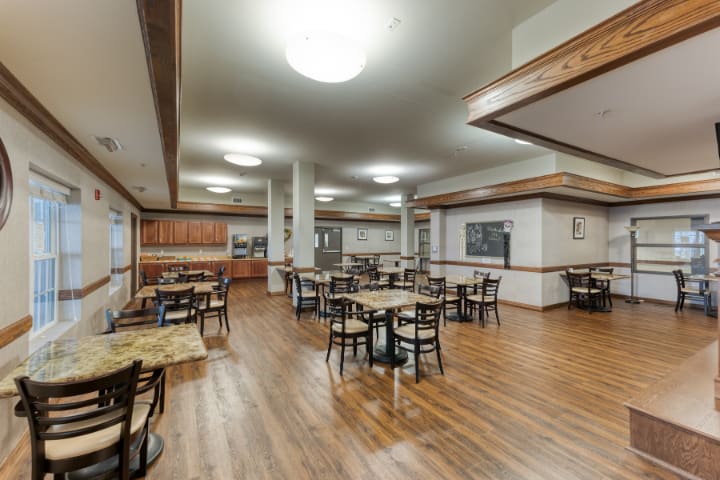 An empty restaurant dining area with wooden floors and neatly arranged tables and chairs.