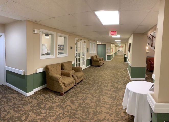 A hallway with comfortable chairs, carpet flooring, and bright lighting.