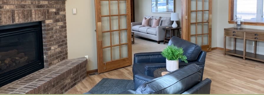 A cozy living room with a comfortable sofa, armchair, and decorative elements like a plant and lamp.