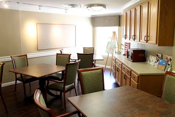 A well-lit meeting room featuring tables, chairs, a whiteboard, and wooden cabinetry.