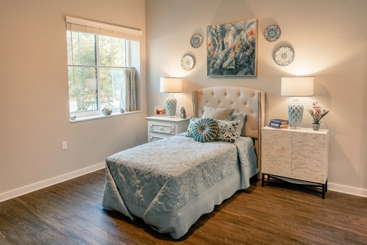 A cozy bedroom with elegant decor, featuring a bed, nightstands, lamps, and artwork on the wall.