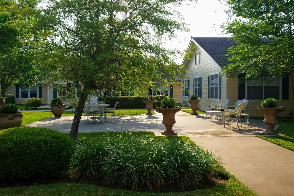 A serene garden patio with seating surrounded by lush greenery and sunshine.