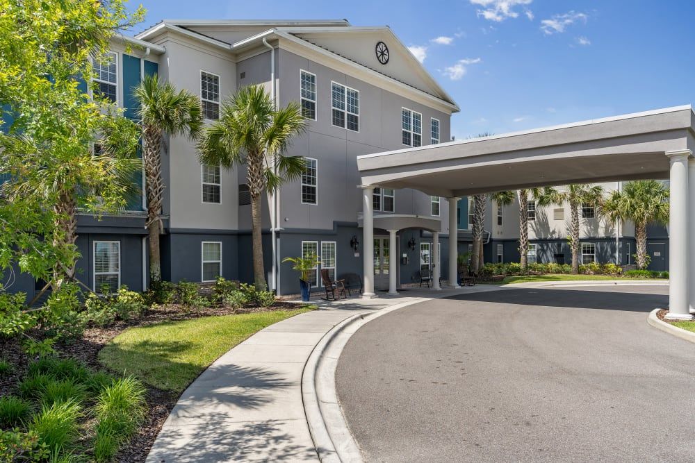 A modern residential building with palm trees and a driveway at the entrance, captured on a sunny day.