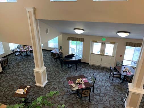 A spacious dining area with neatly arranged tables and chairs, featuring a piano and large windows.