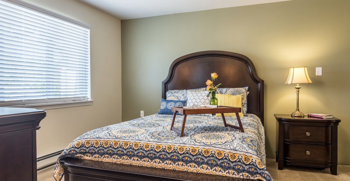 A cozy bedroom with a patterned bedspread and a tray holding flowers.