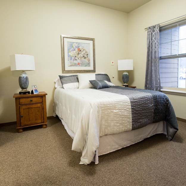 A cozy bedroom with a neatly made bed, nightstands, lamps, and a window.