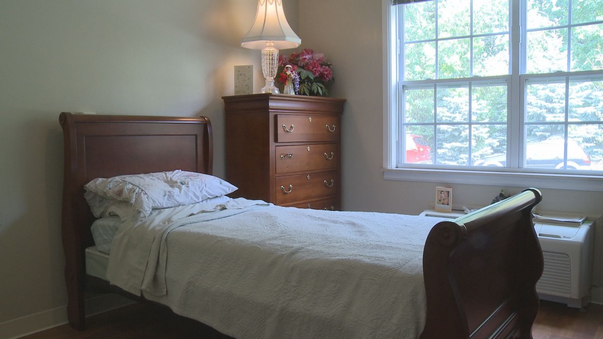 A cozy bedroom with a single bed, lamp, dresser, and window view.
