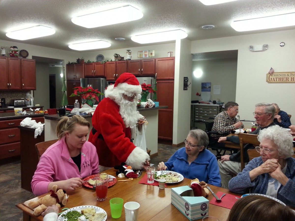 A festive gathering with Santa Claus visiting people during a holiday meal.
