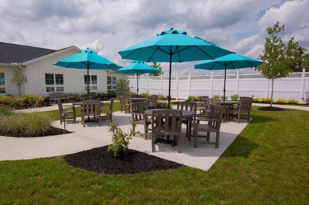 A well-maintained outdoor patio area featuring tables, chairs, and turquoise umbrellas set on a grassy lawn.