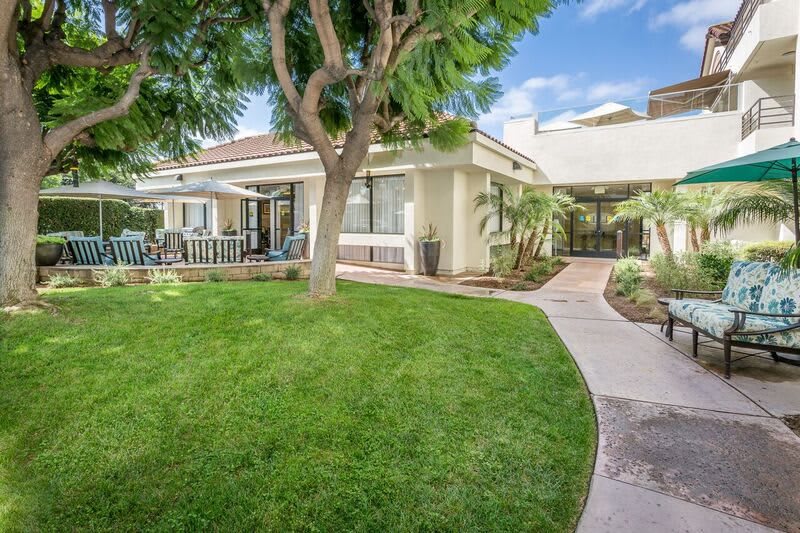A beautiful residential backyard with a well-maintained lawn, trees, and patio.