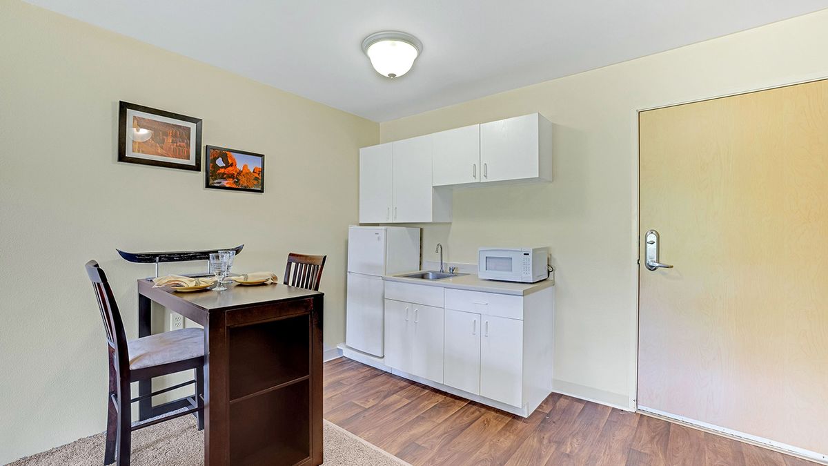 A minimalist apartment kitchen with white cabinets and a small dining area.