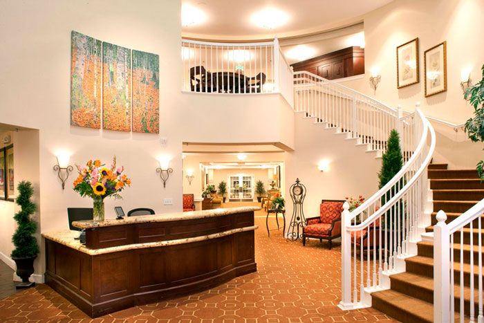 A well-decorated hotel lobby featuring a reception desk, an elegant staircase, and comfortable seating.