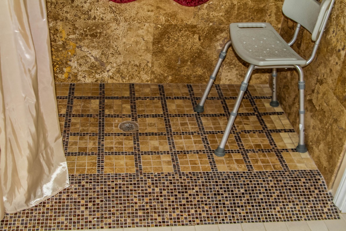 A bathroom with tiled flooring and an accessible shower chair.