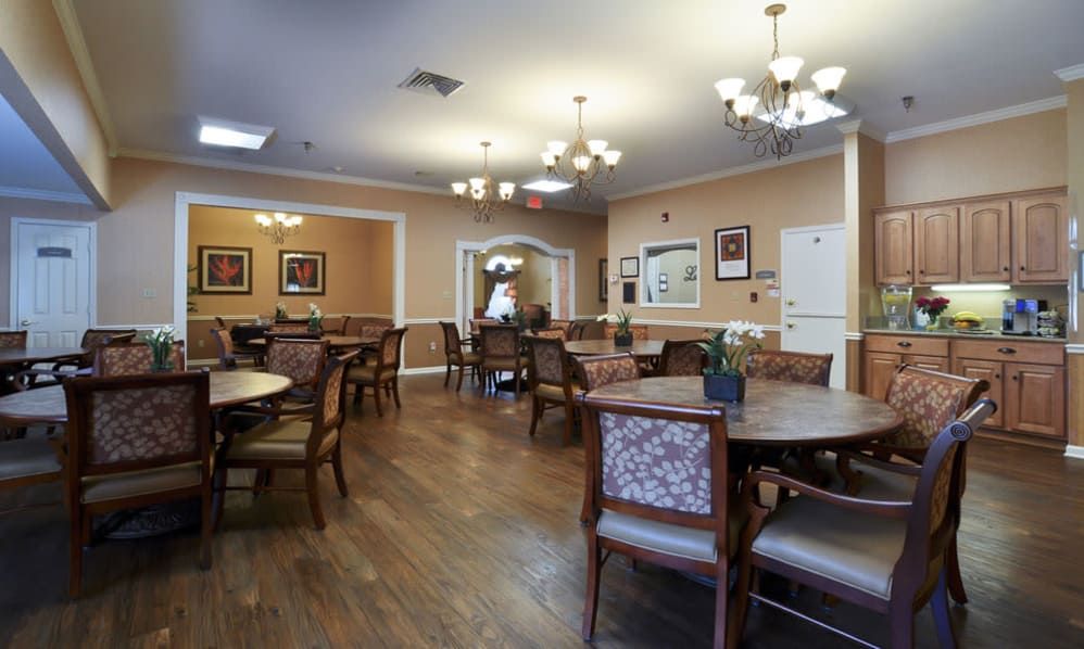 A well-lit dining area with wooden floors, tables, and chairs, decorated with chandeliers and artwork on the walls.