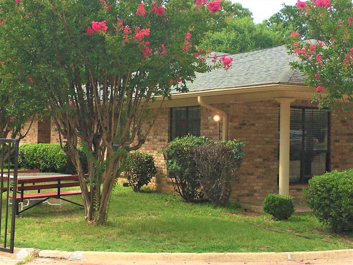 A brick house surrounded by a well-maintained yard with trees and flowers in bloom.