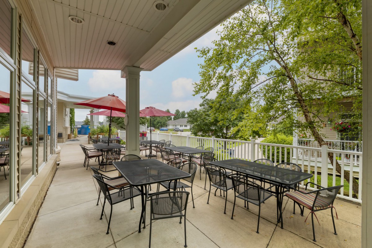 An inviting outdoor patio area with tables and chairs, shaded by umbrellas and surrounded by lush trees.