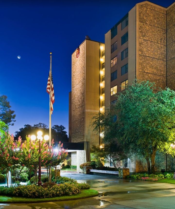 A hotel building illuminated at night with a flag and surrounding trees.