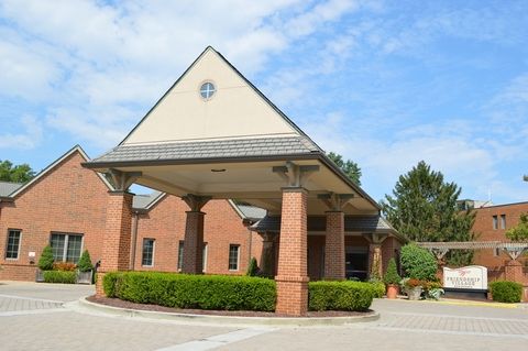 A brick building with a covered entrance and surrounding greenery under a clear sky.