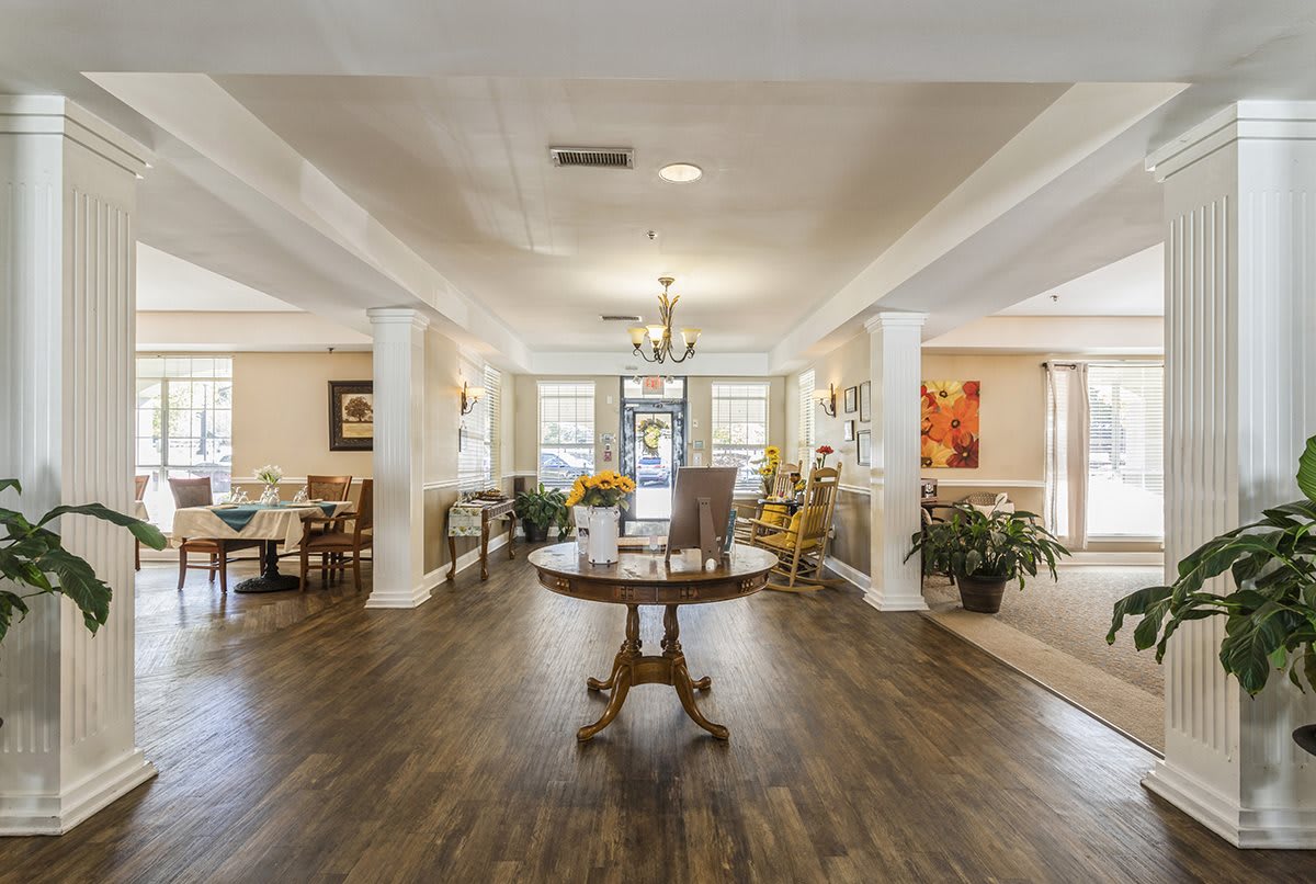 A spacious and elegantly decorated lobby with hardwood flooring, featuring comfortable seating areas and a central table under a chandelier.