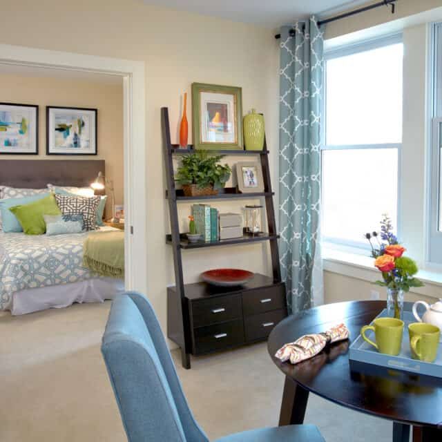 A cozy apartment interior featuring a small dining table, comfortable seating, and a view into the bedroom with stylish decor.