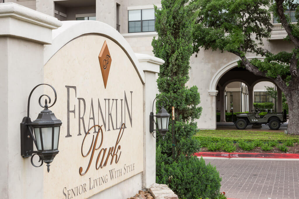 Entrance sign for Franklin Park with surrounding greenery and a view of the building in the background.