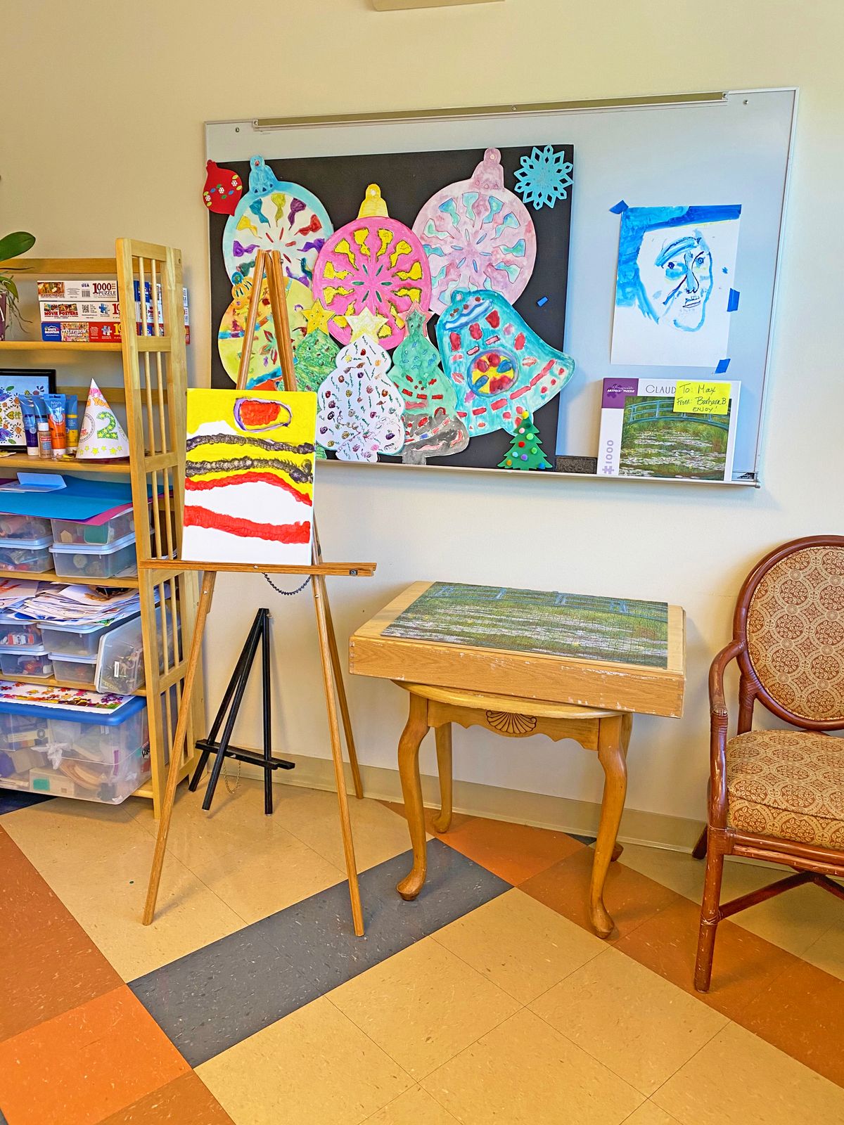 A classroom corner displaying colorful children's artwork on an easel and bulletin board, with a small table and chair nearby.