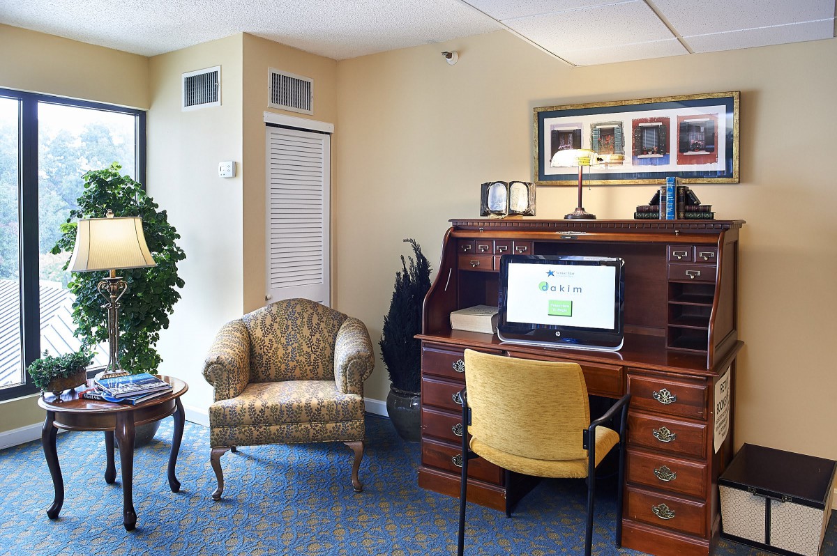 A cozy office space featuring a wooden desk with a computer, armchair, and decorative plants.