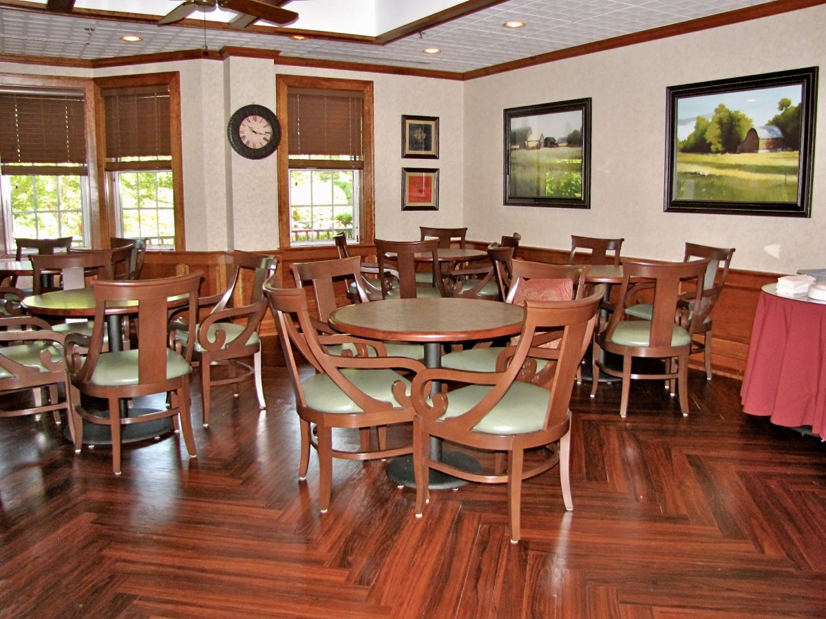 A cozy dining area with wooden flooring, surrounded by tables and chairs, adorned with wall art.