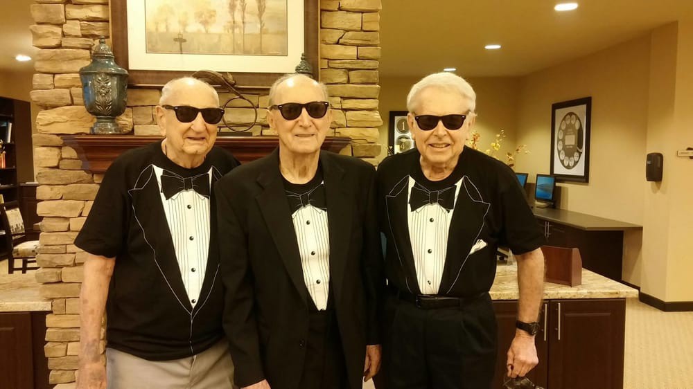 Three elderly men wearing tuxedo print shirts and sunglasses, posing indoors.