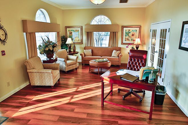 A cozy and well-furnished living room with wooden flooring, featuring sofas, armchairs, a coffee table, and large windows.