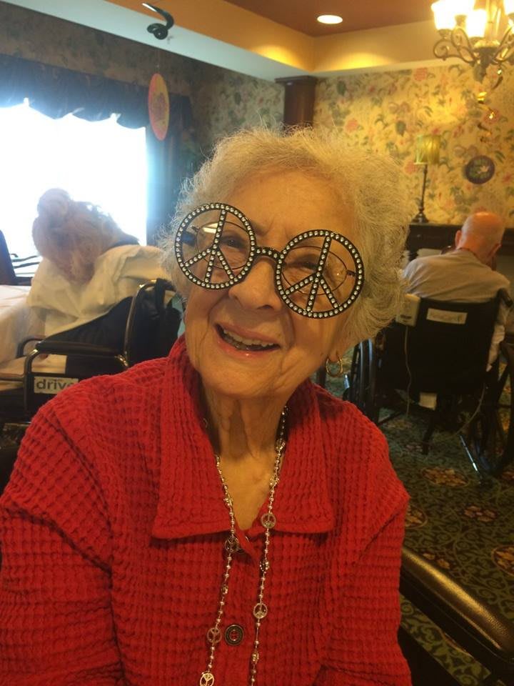 Elderly woman smiling while wearing fun glasses indoors.