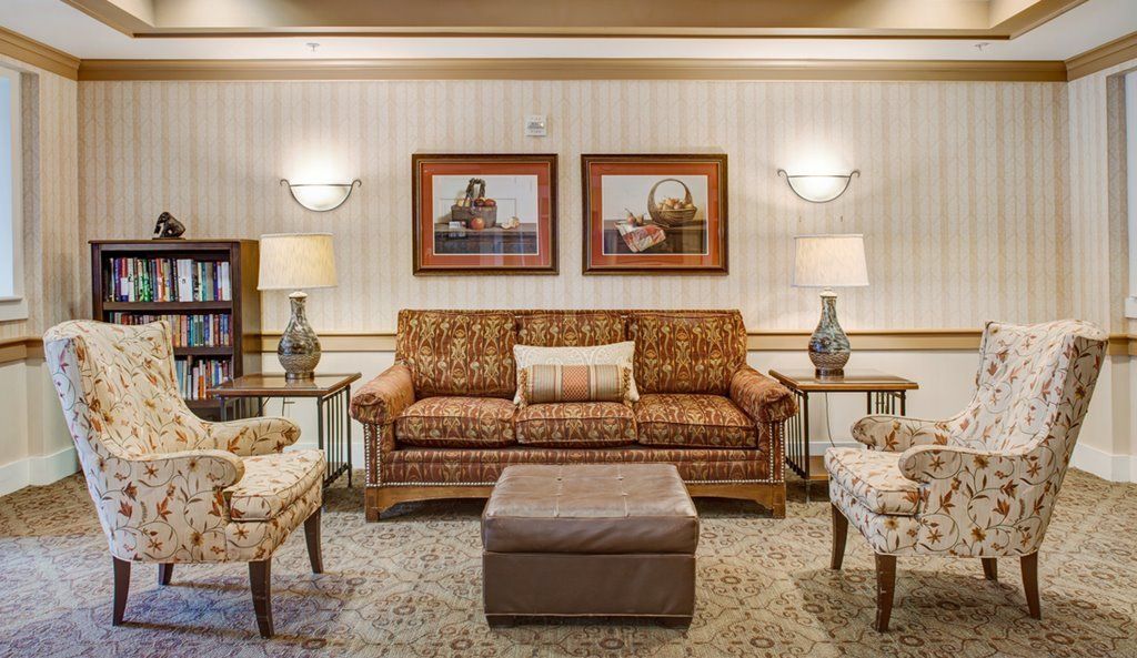 A cozy living room with a patterned sofa, two armchairs, and a central ottoman, elegantly decorated with lamps and artwork on the wall.