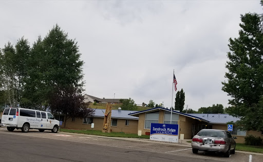 A community building under a cloudy sky, featuring a flag and visible vehicles in the foreground.
