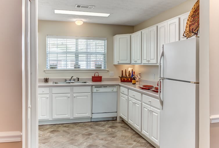 A modern kitchen with white cabinets, featuring a refrigerator, dishwasher, and spacious countertop.