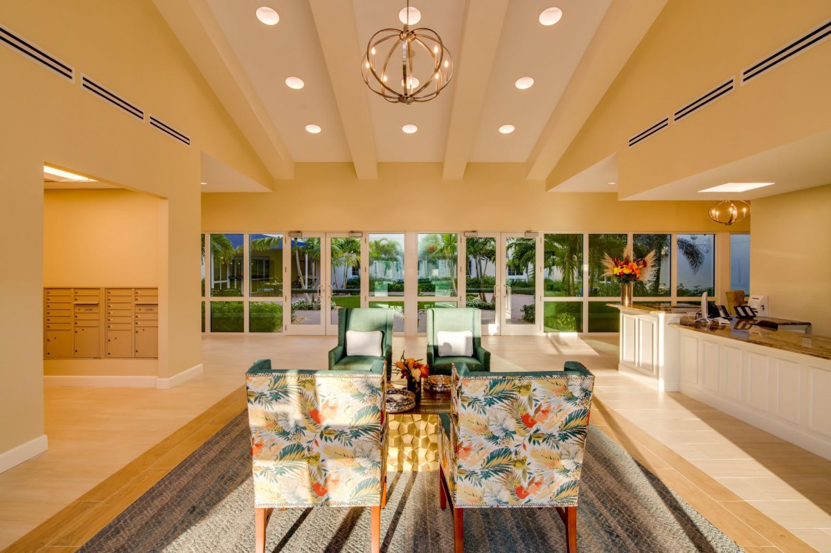 A modern living room with large windows, featuring floral chairs and a central chandelier.