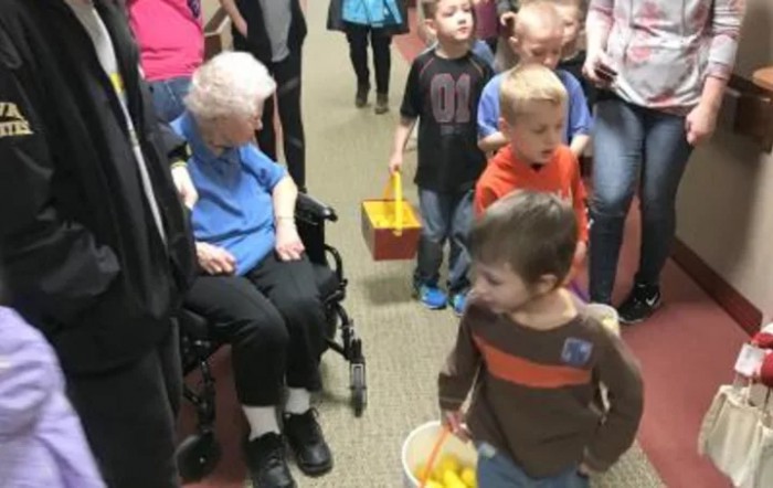 Children engage with an elderly woman in a wheelchair during an indoor event.