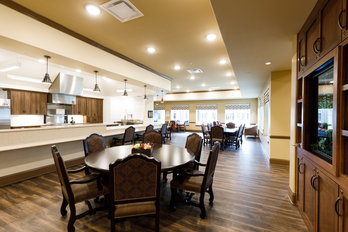 A spacious and well-lit dining area with round wooden tables and upholstered chairs.