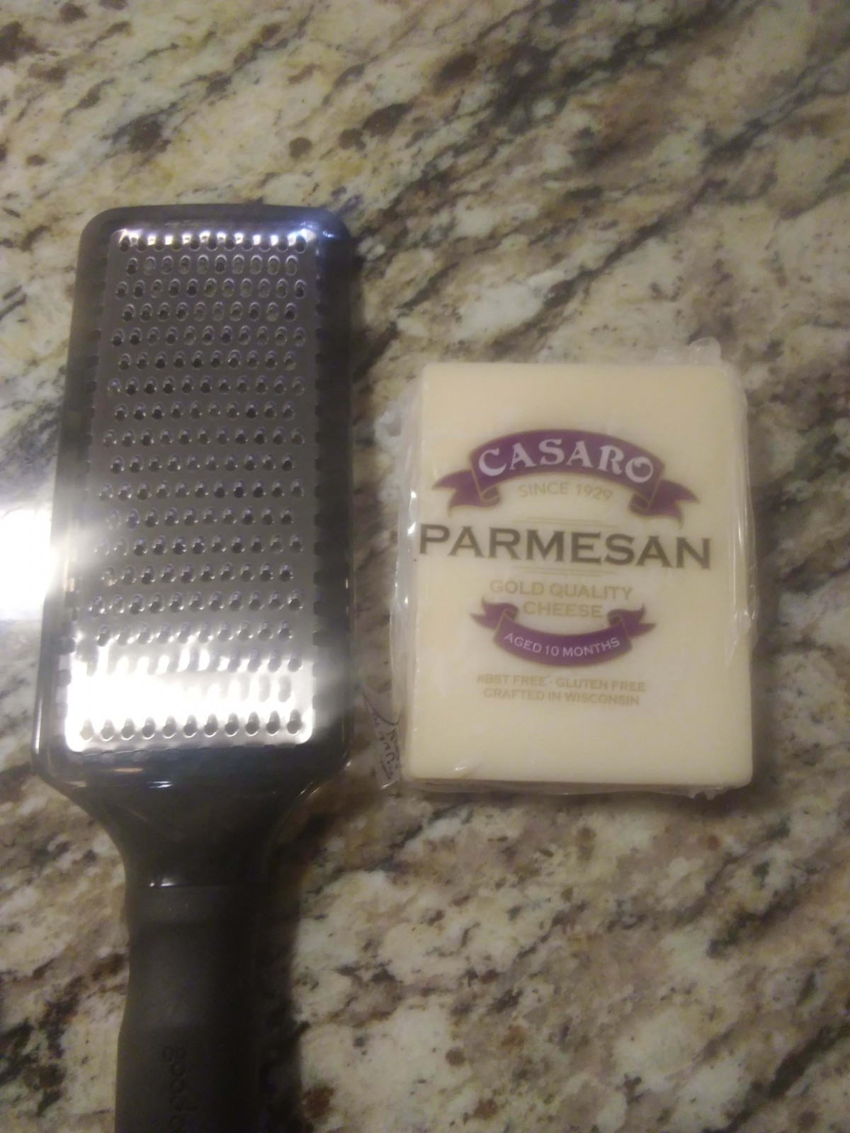 A block of Parmesan cheese next to a grater on a countertop.