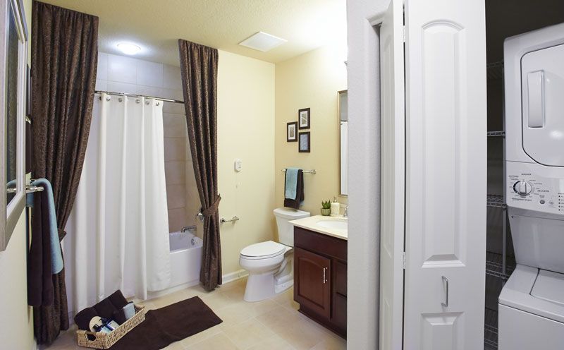 A modern bathroom with beige walls, featuring a shower curtain, toilet, sink with vanity, and mirror.