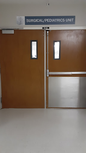 A set of double wooden doors with glass windows, featuring a metal panel, commonly found in a hospital or institutional setting.
