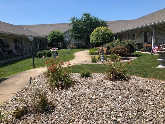 A well-maintained courtyard featuring a pathway, bushes, and trees under a clear blue sky.