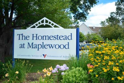 Entrance sign for The Homestead at Maplewood surrounded by colorful flowers and lush greenery.